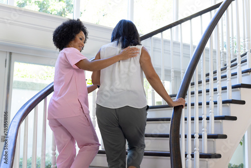 Mature biracial nurse assisting biracial woman up stairs at home