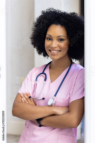 Biracial nurse standing at home, arms crossed, wearing pink scrubs