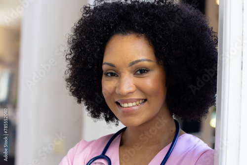 Biracial young woman wearing scrubs and stethoscope, smiling at home