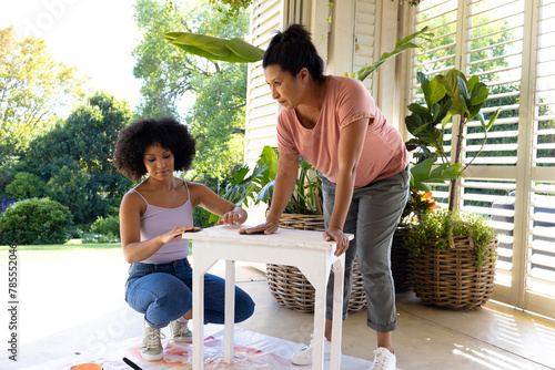 Biracial mother and adult daughter are painting furniture outside at home as an upcycling project