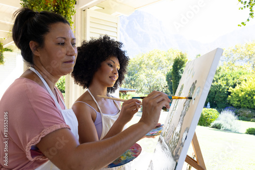 Biracial mother and adult daughter are painting together outdoors, at home