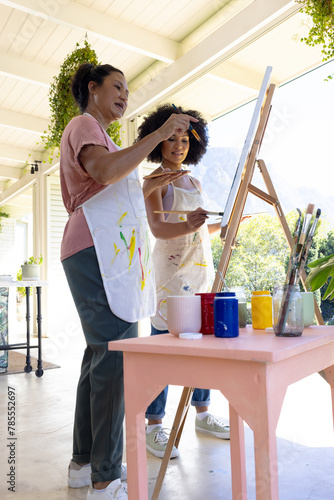 Mother and Daughter, mature biracial woman painting with young biracial woman outdoors at home