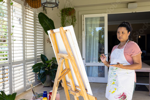 Mature biracial woman painting on canvas at home