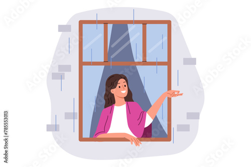 First autumn rain brings joy to woman looking out of apartment window and catching drops with smile. Happy girl enjoying view of street during rain, standing with blanket on shoulders in cozy home