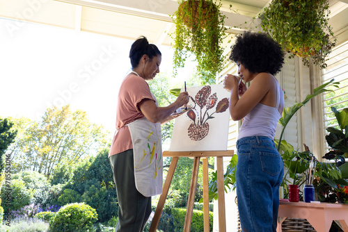 Mature biracial woman and young biracial woman painting together on porch at home