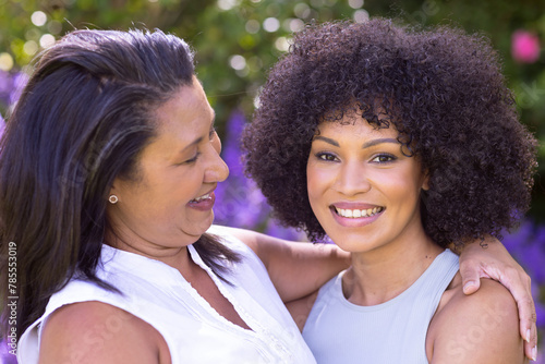 Biracial mature woman and young adult adult daughter are embracing at home
