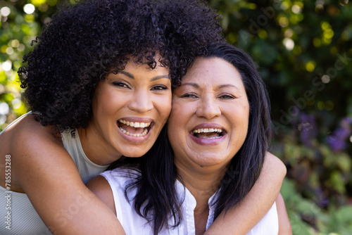Biracial mother and adult daughter are laughing together outdoors at home in the garden