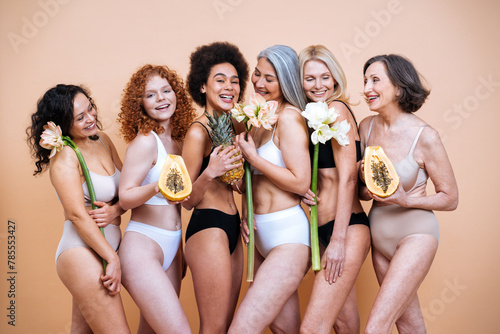Beauty image of a group of women with different age and body posing in studio for a body positive photoshooting. Mixed female models in lingerie on colored backgrounds holding flowers.