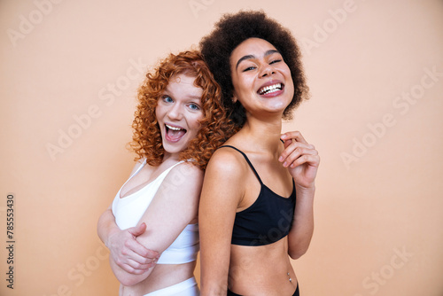 Beauty image of two young smiling and happy women with different body posing in studio for a body positive photoshooting. Mixed female models in lingerie on colored backgrounds. 