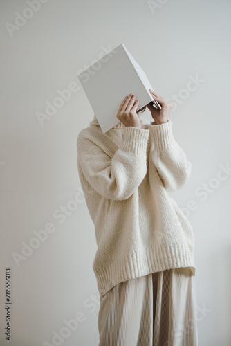 Woman in white wearing hiding face with book, album or notebook. Reading, studying concept. Neutral beige color. Blank cover sheet mock up with copy space