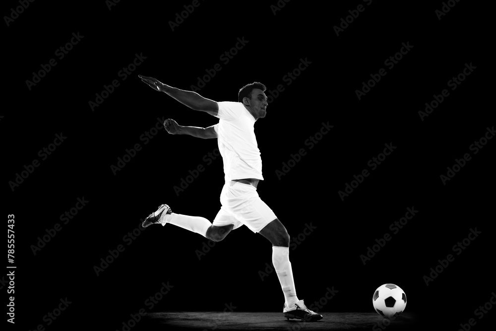 Creative image of young man in white uniform, football player in motion with ball on black background, Monochrome. Professional sport, game, competition, tournament, action, active lifestyle concept Creative image of young man in white uniform, football player in motion with ball on black background, Monochrome. Professional sport, game, competition, tournament, action, active lifestyle concept