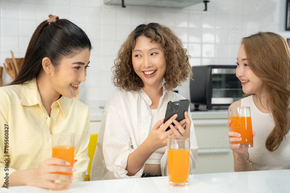 Three women engaging with a smartphone and enjoying orange juice together in a home kitchen. Three women engaging with a smartphone and enjoying orange juice together in a home kitchen.