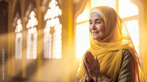 Senior Arab woman, with bright yellow veil, peacefully prays in warmly lit mosque.