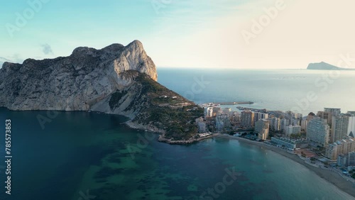 Sunset over Calpe city and Peñón de Ifach mountain. Drone tracking right above the bay. Sunset colours reflecting on buildings and mountain. Travel destination in Spain, Alicante Province.