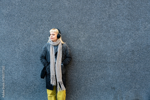 Tableau sur toile Portrait of young confident independent stylish hipster woman standing against black wall with wireless headphones listening music while waiting