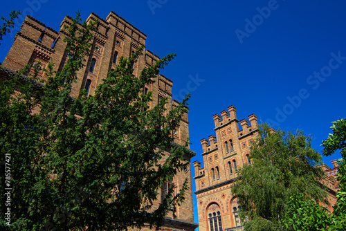 Chernivtsi National University, Residence of Bukovinian and Dalmatian Metropolitans in the city of Chernivtsi, Ukraine. Red brick facade with green trees and bushes at sunny day. UNESCO
