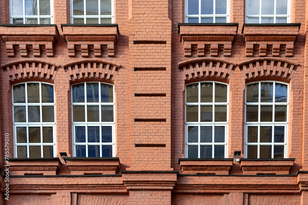Fragment of facade of old classic red brick building with four large windows with white frames
