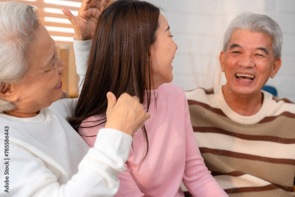 Fototapeta premium Asian Family Bonds: Daughter's Laughter Echoes in the Home as Grandfather and Grandmother Enjoy Retirement, Sharing Hugs and Smiles on the Sofa, A Precious Elderly Bonding Moment