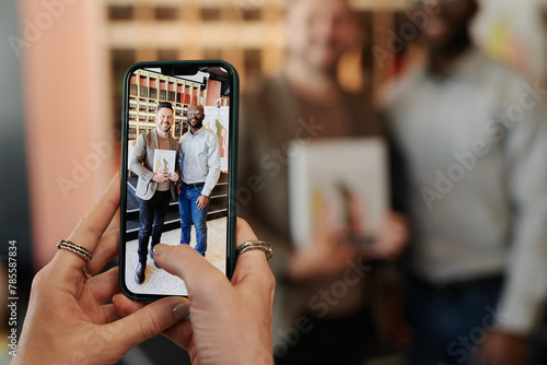 Smartphone in hands of young woman taking picture of male writer and his fan holding new book with author autograph photo