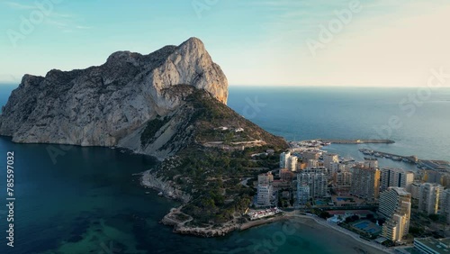 Aerial view of Peñón de Ifach mountain. Beautiful warm colours reflecting on the mountain peak at sunset. Natural Park in Calpe city, Alicante Province. View of part of the Calpe city. Drone backwards photo