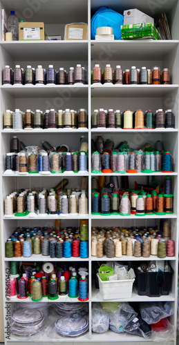 A large open cabinet is filled with bobbins with threads of different colors and details at the sewing facility. Shelves with new threads for the manufacture of upholstered furniture covers