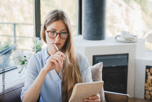 Young pensive woman making to-do list and taking notes at home. Freelancer businesswoman creating new ideas, startups, writing shopping list in the notebook indoors