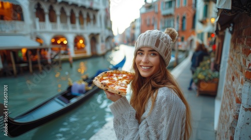 Cheerful young female traveler enjoys a delicious slice of traditional Italian pizza while exploring the enchanting city of Venice, overlooking a beautiful canal with historical architecture.