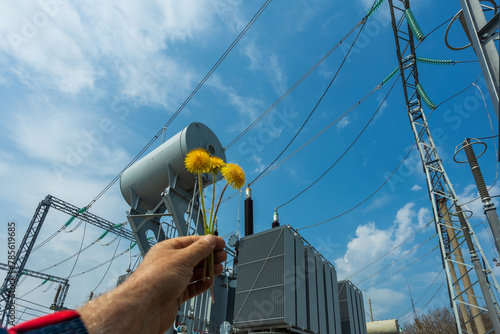 Three-phase high-voltage transformer of high electrical power with high-voltage bushings at a substation against the background of a blue sky and yellow dandelions. photo