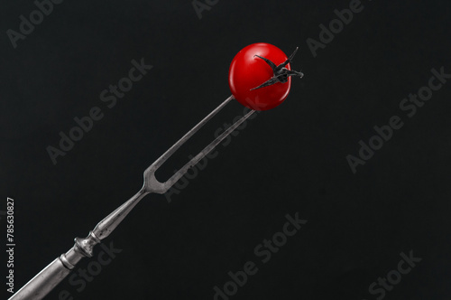 Cherry tomato prickled by a vintage fork on black background © unclepodger