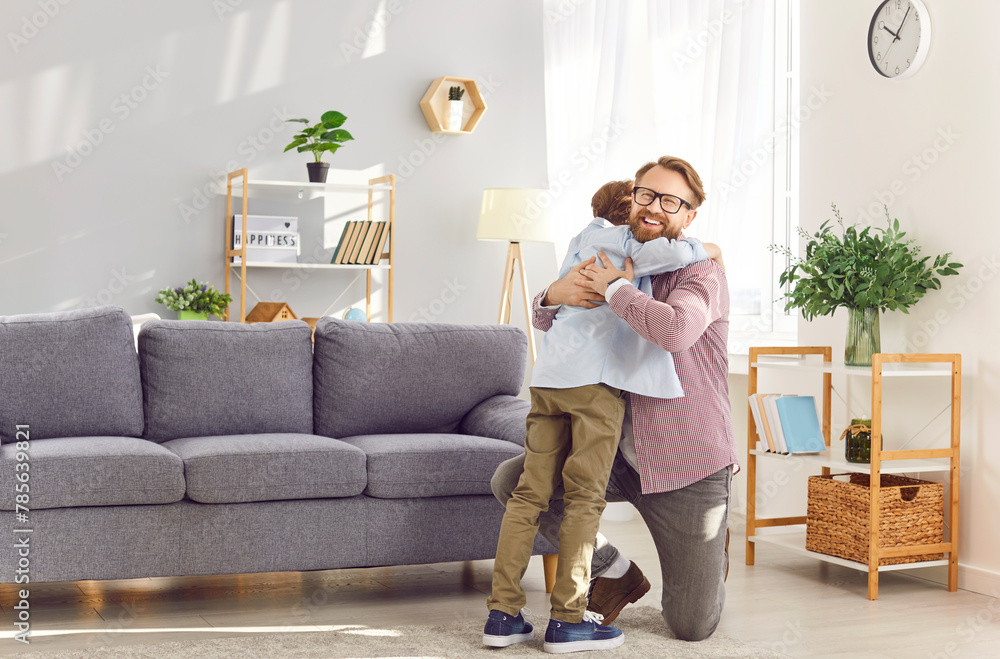 Caucasian bearded father embraces his young son in the living room at home, smiling and happy, illustrating the love between parent and child. A heartwarming moment for father's day.