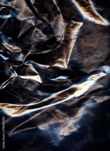 Creased surface. Crumpled material. Black color metallic overlay light refraction wrapped foil worn aged film glow texture grunge abstract background.