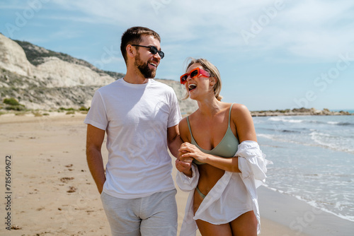 Photography Young attractive couple laughs as they walk along the beach