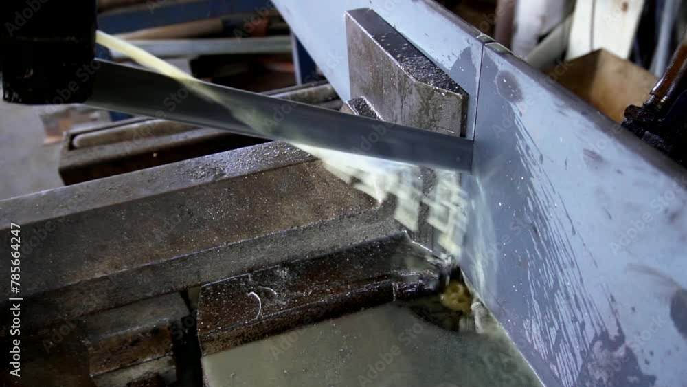 An automatic band saw cuts metal using a water-based coolant. Industrial machine. An automatic band saw cuts metal using a water-based coolant. Industrial machine.