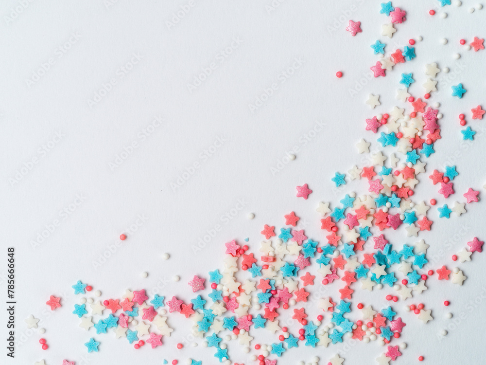 Festive border frame of colorful pastel sprinkles on white background with copy space one edge. Sugar sprinkle dots and stars, decoration for cake and bakery. Top view or flat lay