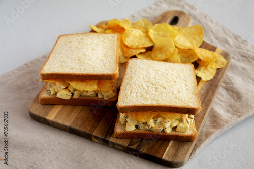 Homemade Egg Salad Sandwich with Potato Chips on a wooden board, side view.