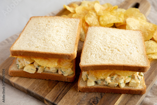 Homemade Egg Salad Sandwich with Potato Chips on a wooden board, side view.