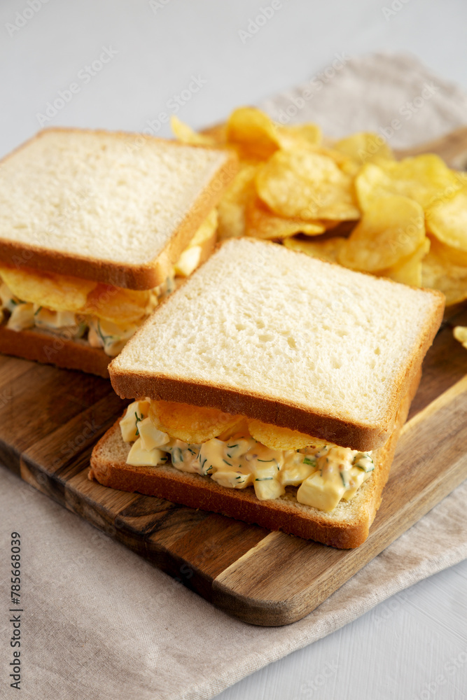 Homemade Egg Salad Sandwich with Potato Chips on a wooden board, side view.