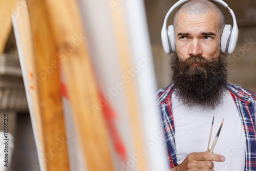 Moving paint brush artist works on abstract oil painting in creative modern studio. Guy with headphones listening to music. Abstract Modern Art.