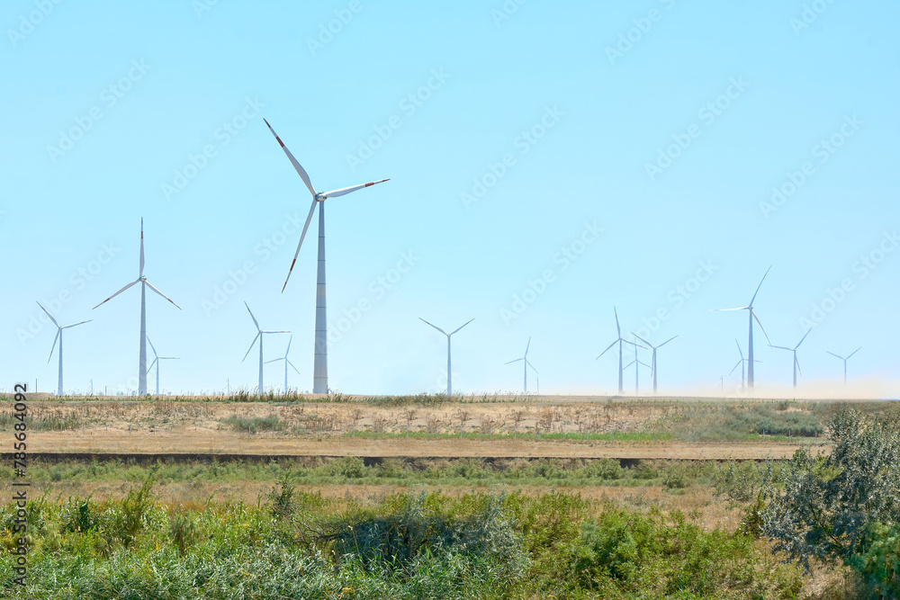 View of wind power plants in a field, against the blue sky.