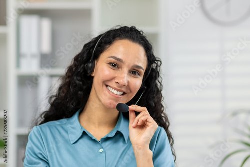 A cheerful woman with a headset engaging in a friendly video call  looking directly at the camera  possibly providing customer support or virtual assistance from an office.