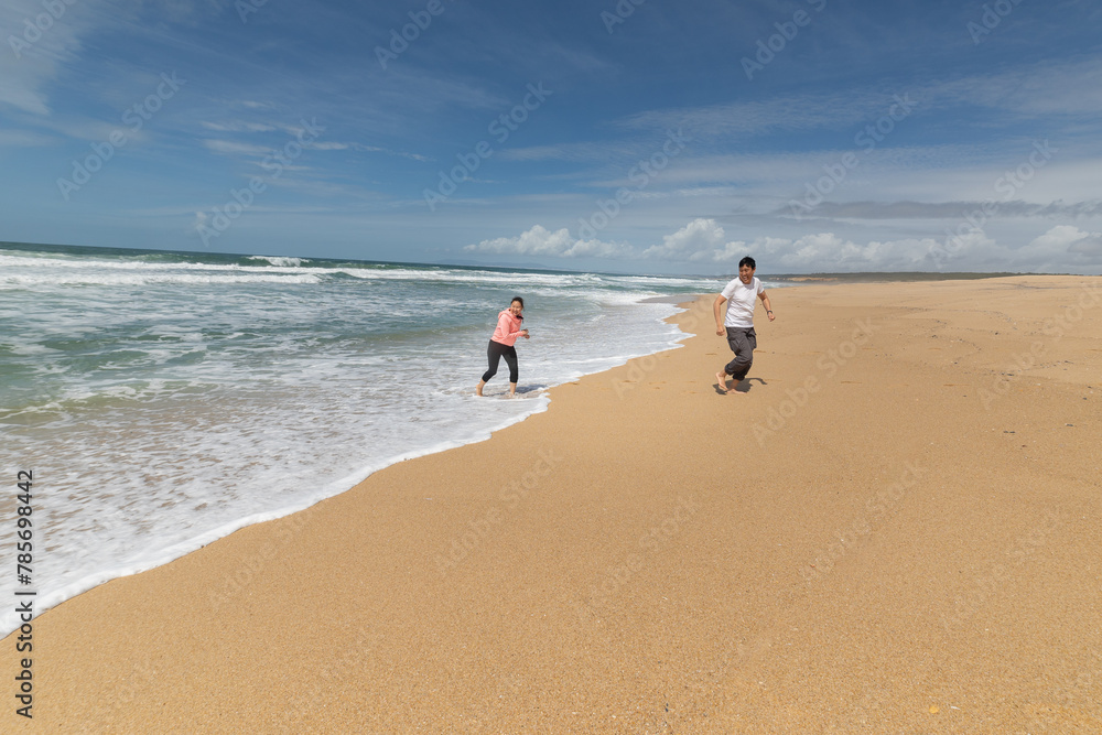 Two people are running on a beach with the ocean in the background