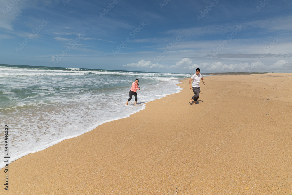 Two people are running on a beach with the ocean in the background Two people are running on a beach with the ocean in the background