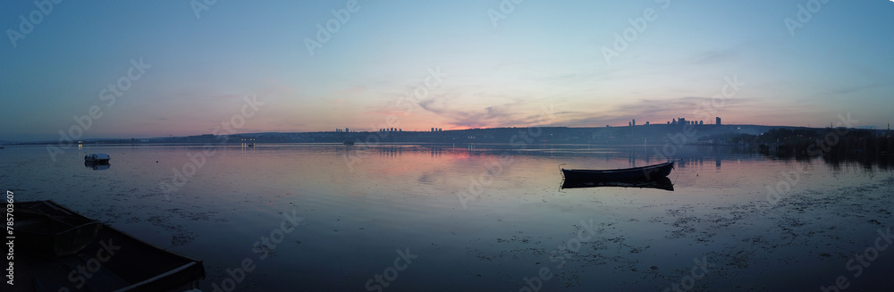 A boat is floating on a lake at sunset. The sky is filled with clouds and the sun is setting A boat is floating on a lake at sunset. The sky is filled with clouds and the sun is setting