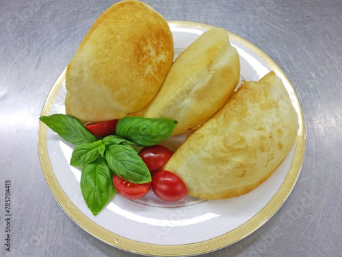 pasties with meat on a large white plate. delicious fluffy pastries served with cherry tomatoes and fresh basil sprigs