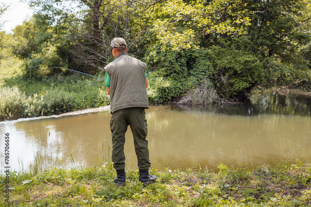 Young man, a freshwater fisherman holding a fishing rod with a spinning reel, getting ready to catch a fish. Fishing equipment and skills concepts. Young man, a freshwater fisherman holding a fishing rod with a spinning reel, getting ready to catch a fish. Fishing equipment and skills concepts.