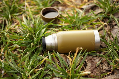 A green cylinder Drinkware lies on the grass next to a cup