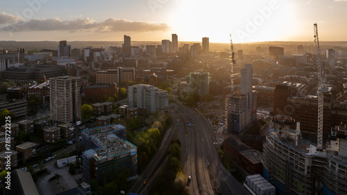 The sun pierces the morning sky, casting a serene glow over Leeds, emphasizing the construction and architectural landscape of the busy city centre from a drone's view