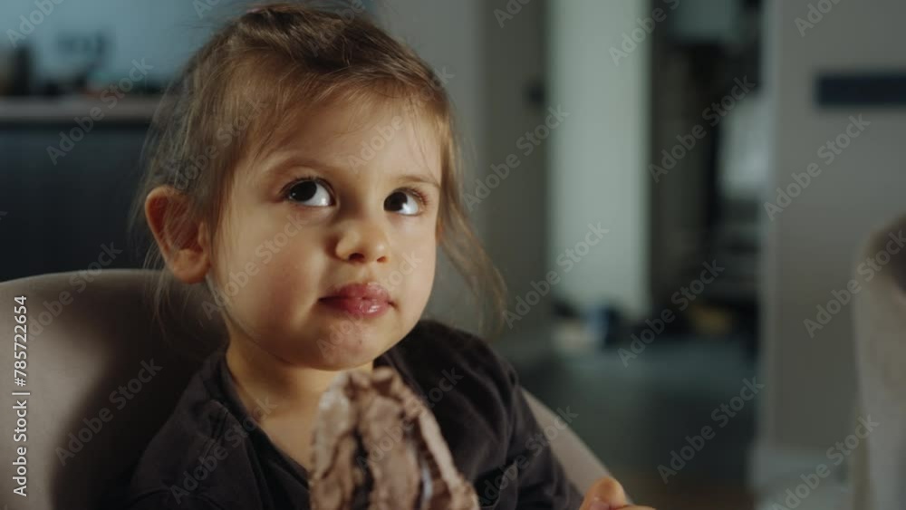 Happy girl eating ice cream cone smiling while resting in high-chair at home. Child enjoying ice cream indoors. Happy holidays, summertime Happy girl eating ice cream cone smiling while resting in high-chair at home. Child enjoying ice cream indoors. Happy holidays, summertime