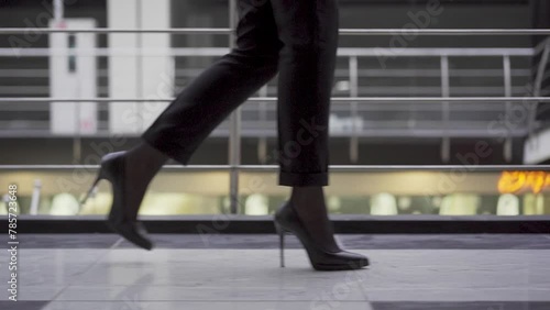 Side profile shot business woman wearing stylish high heels and steps into workspace. Slim female legs in black stilettos walking in office hallway. Feet of young successful business woman in high