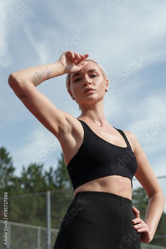 A strong athletic woman rests with her hand on her head against a clear sky backdrop, showcasing determination and wellness.